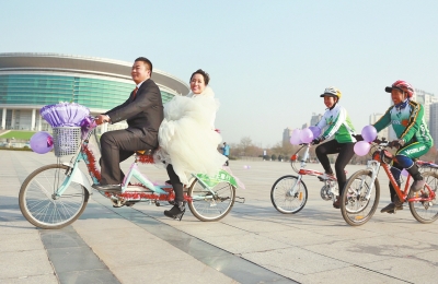 氣球和鮮花裝點(diǎn)的雙人自行車，新郎郝幸福載著美麗新娘回家。