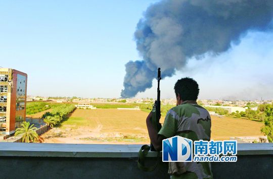 2日，利比亞首都的黎波里，一民兵武裝成員眺望被火箭彈擊中的儲油罐冒出濃煙。