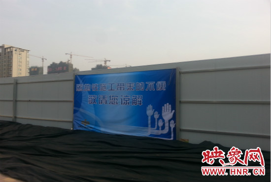 道路南側(cè)圍起了白色的圍擋，墻上標(biāo)示著“因地鐵施工帶來(lái)的不便敬請(qǐng)您諒解”的提示牌。