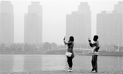 29日中午，鄭東新區(qū)如意湖畔，兩個(gè)年輕人拍攝霧霾中的景色。 鄭州晚報(bào)記者 馬健 圖