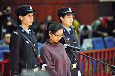 被告人盧梅低著頭，站在朝陽法院刑事審判庭的被告席上。